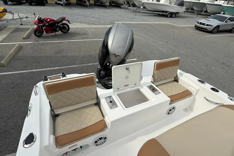 Slide: The Image of 2025 NauticStar 191 Hybrid boat interior with tan seating and motor in parking lot. - 18