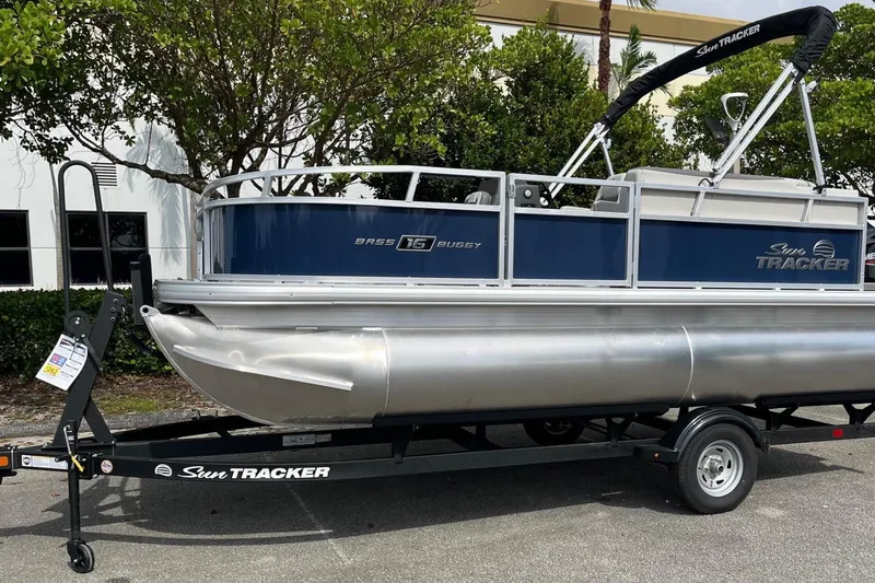 Slide: The Image of 2026 Sun Tracker Bass Buggy 16 XL Select pontoon boat on trailer, parked outdoors. - 2