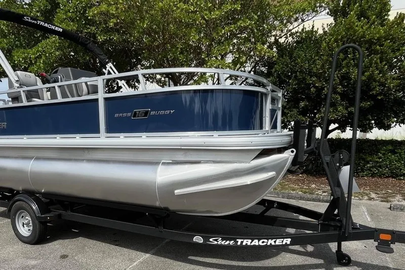 Slide: The Image of 2026 Sun Tracker Bass Buggy 16 XL Select pontoon boat on trailer, parked outdoors. - 3