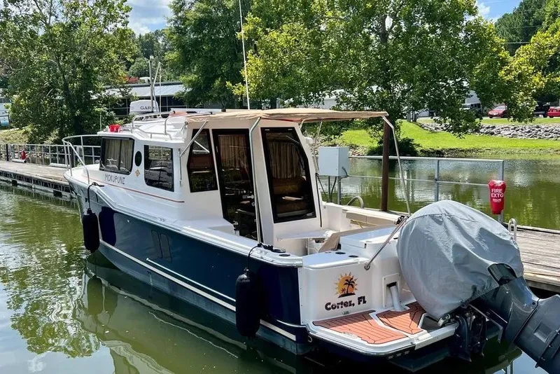 Slide: The Image of 2022 Ranger Tugs R-27 boat docked by a scenic lakeside with lush greenery. - 2