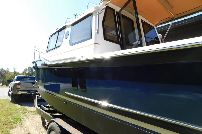 Slide: The Image of 2022 Ranger Tugs R-27 boat on trailer, parked beside a pickup truck. - 55