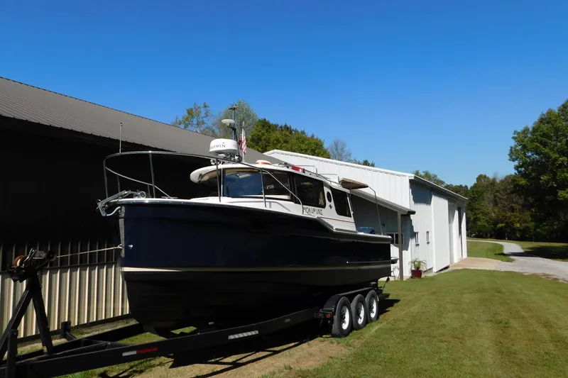 Slide: The Image of 2022 Ranger Tugs R-27 boat on trailer beside a white building under clear blue sky. - 63