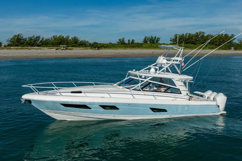 Slide: The Image of 2023 Intrepid 477 Evolution boat cruising on clear blue water near a sandy beach. - 11