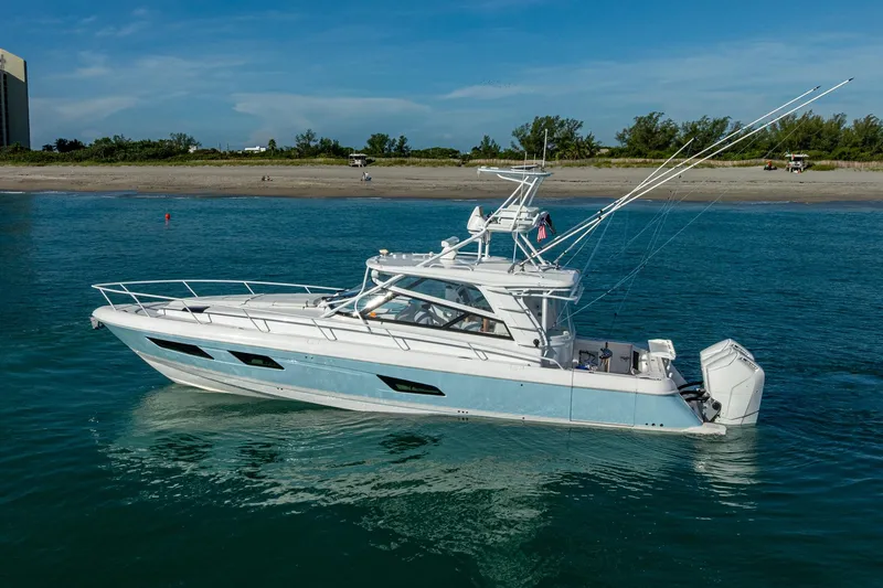 Slide: The Image of 2023 Intrepid 477 Evolution yacht cruising on clear blue water near a sandy beach. - 6