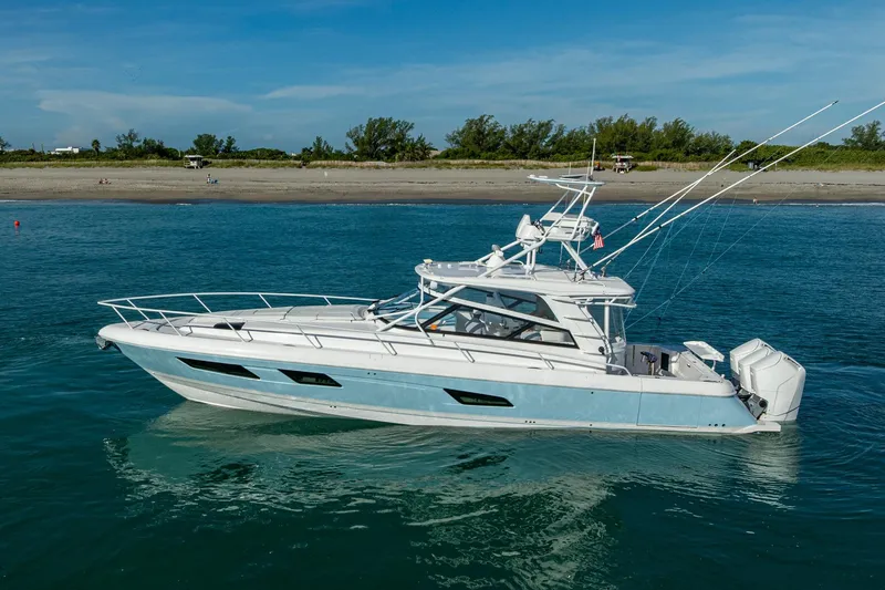 Slide: The Image of 2023 Intrepid 477 Evolution yacht cruising near a sandy shoreline under a clear blue sky. - 7