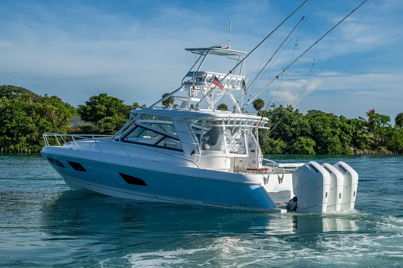 Slide: The Image of 2023 Intrepid 477 Evolution boat cruising on clear blue water near lush greenery. - 81