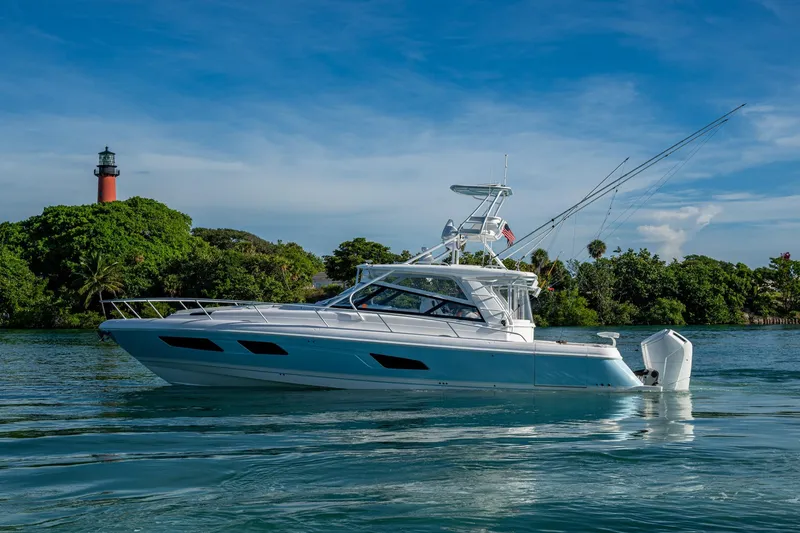 Slide: The Image of 2023 Intrepid 477 Evolution yacht cruising near a lighthouse and lush greenery. - 84