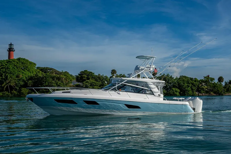 Slide: The Image of 2023 Intrepid 477 Evolution yacht cruising near lush green shoreline. - 85