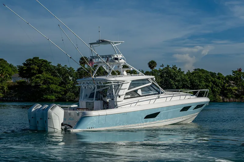 Slide: The Image of 2023 Intrepid 477 Evolution yacht cruising on a sunny day near lush greenery. - 88