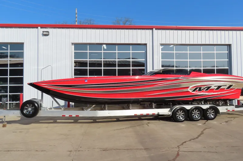 The Image of Red 2010 MTI 36 R/P speedboat on trailer, parked outside a garage. - 0