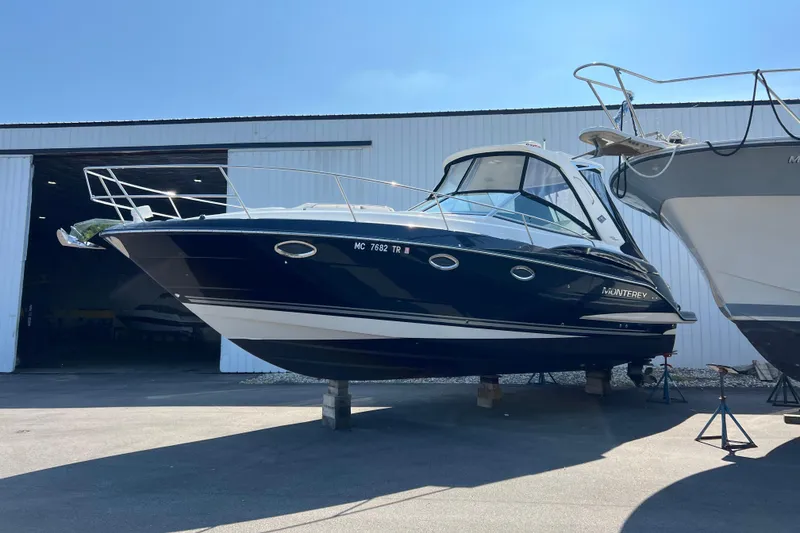The Image of 2014 Monterey 320 Sport Yacht in storage, sleek design, black hull, outdoor setting. - 0