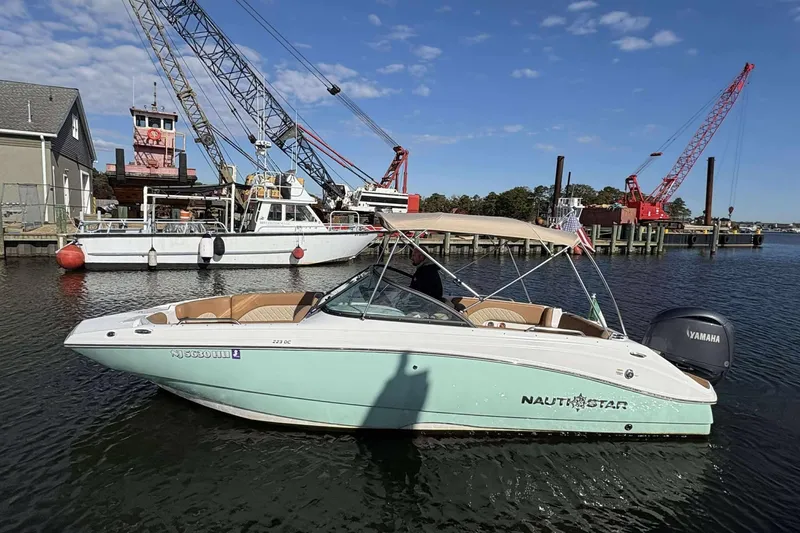 The Image of 2024 NauticStar 223 DC boat docked near cranes and industrial buildings. - 1