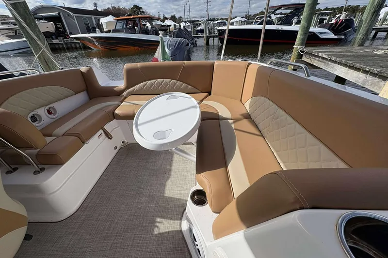 Slide: The Image of 2024 NauticStar 223 DC boat interior with tan seating and round table in marina setting. - 11