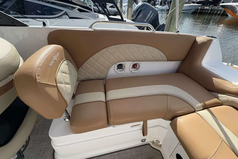 Slide: The Image of 2024 NauticStar 223 DC boat interior with tan and cream seating, docked by the water. - 15