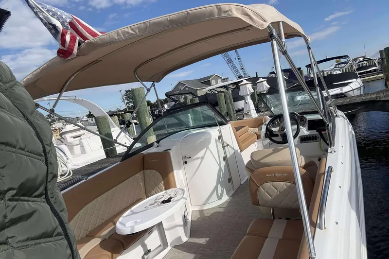 Slide: The Image of 2024 NauticStar 223 DC boat with tan seating and canopy at a marina. - 18