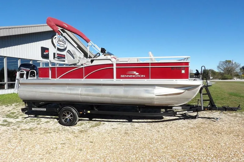 Slide: The Image of 2022 Bennington 20 SVF pontoon boat with red accents on a trailer, outdoors. - 5