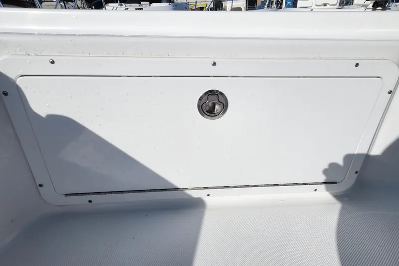 Slide: The Image of 2026 Savannah 220 IS boat storage compartment with latch, white finish, outdoor setting. - 17