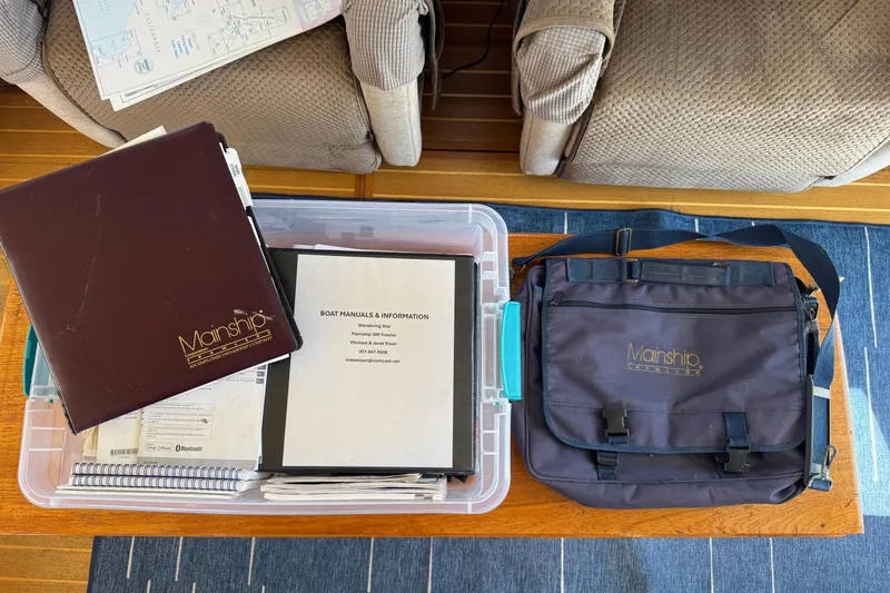 Slide: The Image of Mainship 390 Trawler 2000 manuals and bag on a wooden table. - 81