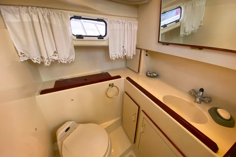 Slide: The Image of Camano 30 boat bathroom with sink, toilet, mirror, and window with lace curtains. - 26