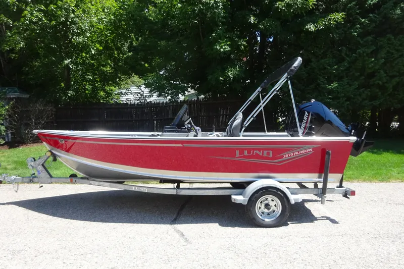 The Image of 2024 Lund 1675 Alaskan SS boat on trailer, red exterior, parked outdoors. - 0