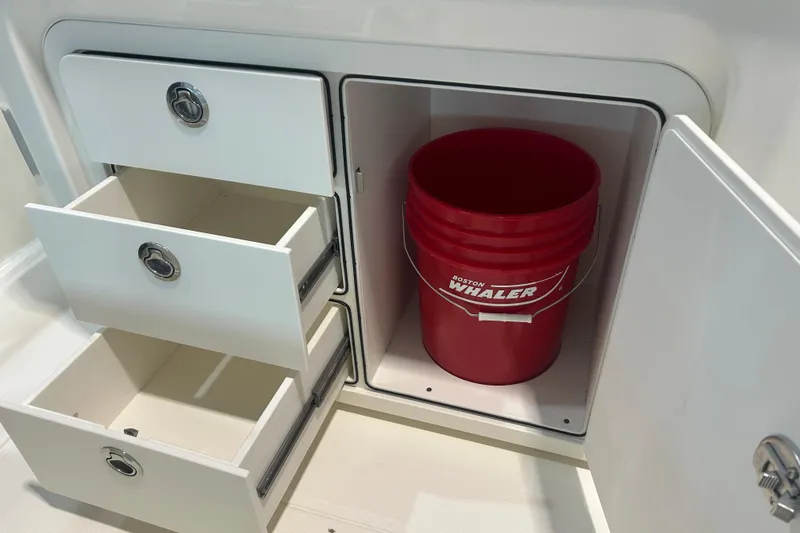 Slide: The Image of Storage area with drawers and a red Boston Whaler bucket on a 2025 220 Dauntless boat. - 14