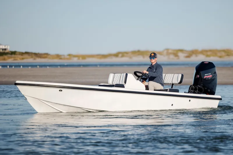 The Image of A person driving a 2026 Vtech 18 boat on calm waters near a sandy shore. - 0