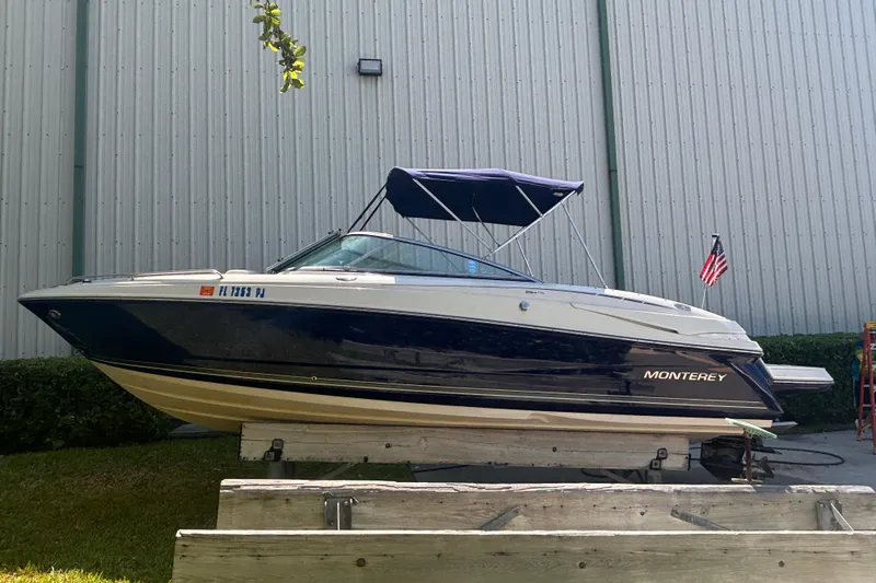 Slide: The Image of 2010 Monterey 254FS boat with blue canopy, docked near a metal building. - 2
