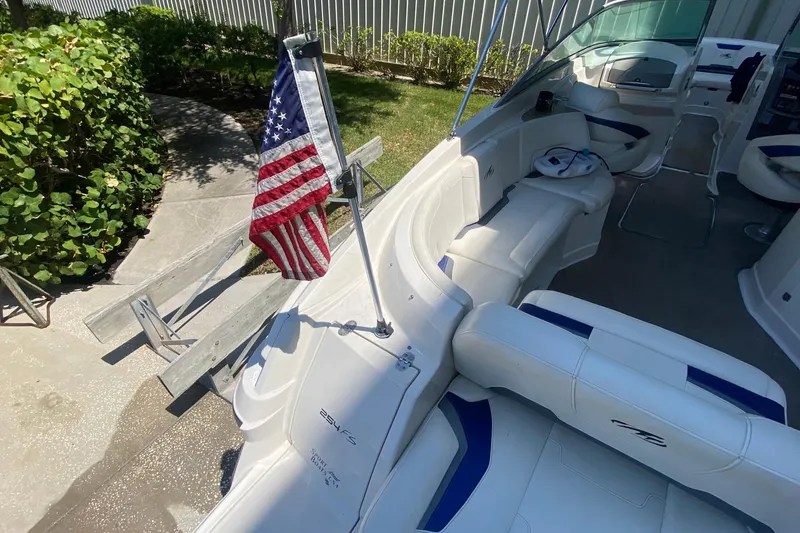 Slide: The Image of 2010 Monterey 254FS boat interior with American flag, white seating, and lush greenery. - 22