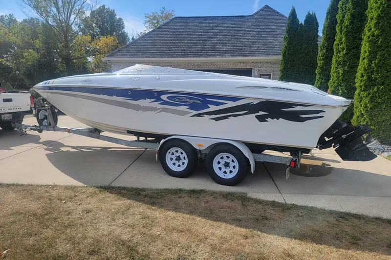 The Image of 2004 Baja H2X boat on trailer, parked in driveway, with blue and black graphics. - 0