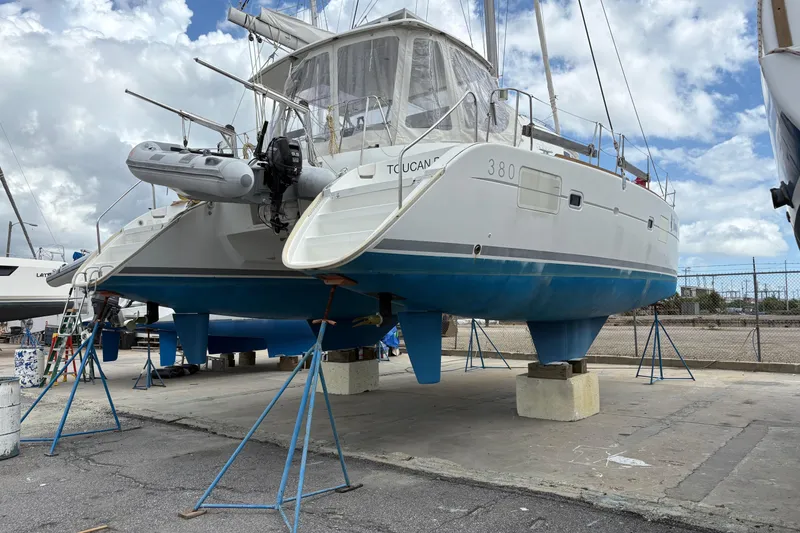 The Image of 2004 Lagoon 380 catamaran on stands, ready for maintenance under a cloudy sky. - 0