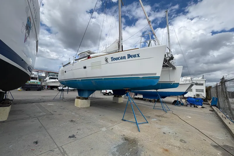 Slide: The Image of 2004 Lagoon 380 catamaran "Toucan Deux" on stands in a boatyard under cloudy skies. - 1
