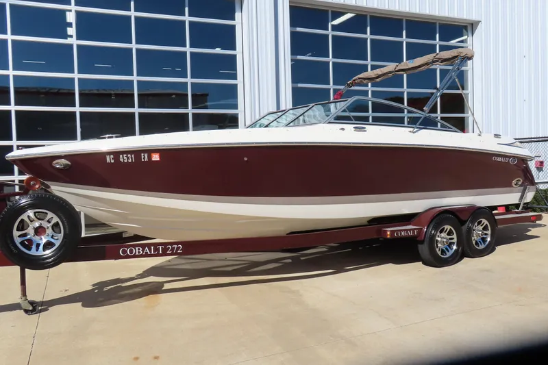 Slide: The Image of 2005 Cobalt 272 boat on trailer, maroon and white, parked outside a building. - 1
