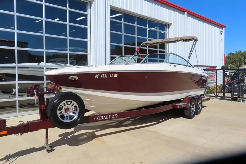 Slide: The Image of 2005 Cobalt 272 boat on trailer, parked outside a building with large windows. - 2