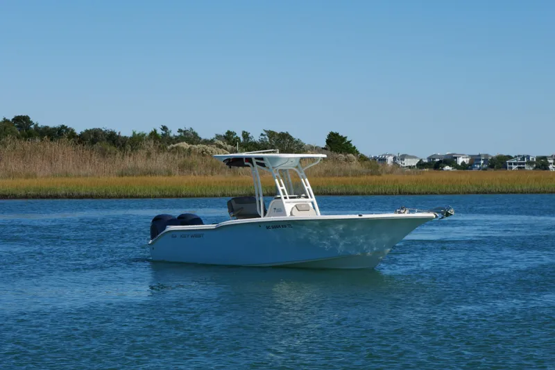 Slide: The Image of 2021 Key West 244 Center Console boat on calm water with grassy shoreline. - 2