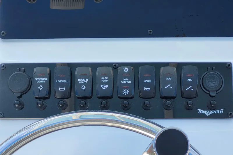 Slide: The Image of Control panel of 2026 Savannah 2200 Offshore boat with labeled switches and steering wheel. - 23