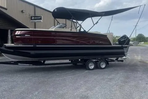 Slide: The Image of 2024 Sylvan G-3 DLZ DC pontoon boat with canopy on trailer, parked outside a building. - 13