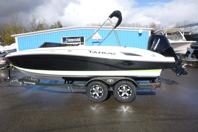 The Image of 2021 Tahoe 210 S boat on trailer, parked outside a blue showroom. - 1