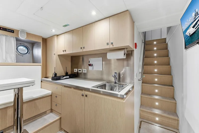 Slide: The Image of Modern yacht interior with kitchenette, wooden cabinets, stairs, and porthole window, Custom Line 106, 2024. - 84