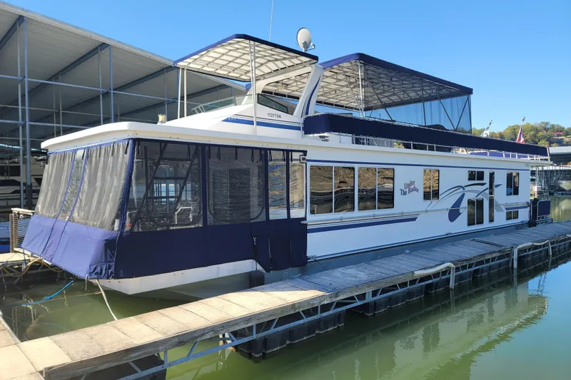Slide: The Image of 2002 Fantasy 16 X 68 Houseboat docked at marina, featuring blue canopy and spacious design. - 2