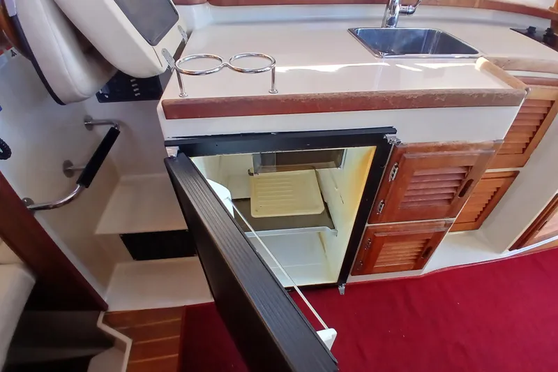 Slide: The Image of 2009 Ranger Tugs R-25 interior with open fridge, sink, and wooden cabinetry. - 18