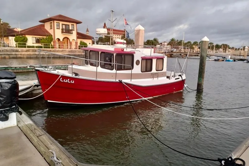 Slide: The Image of 2009 Ranger Tugs R-25 boat docked in a marina, red hull, scenic background. - 2