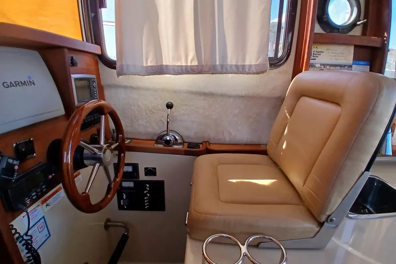 Slide: The Image of 2009 Ranger Tugs R-25 helm with Garmin navigation, wooden steering wheel, and beige captain's chair. - 26