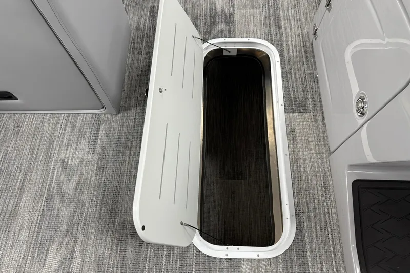 Slide: The Image of 2026 Bentley Pontoons Elite 223 Swingback storage compartment with open hatch on carpeted floor. - 5