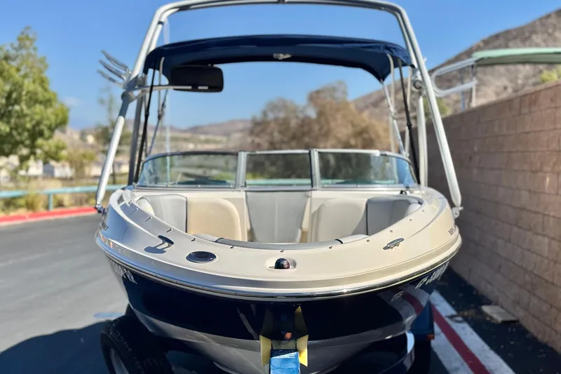 Slide: The Image of 2006 Bayliner 215 Bowrider boat with canopy, parked outdoors on a sunny day. - 2
