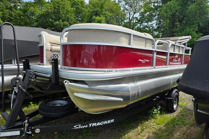 The Image of 2026 Sun Tracker Party Barge 18 DLX pontoon boat on trailer, red and beige design. - 2