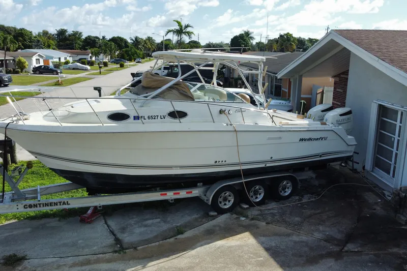 The Image of 2002 Wellcraft 290 Coastal boat on trailer, parked near a house with lush greenery. - 0