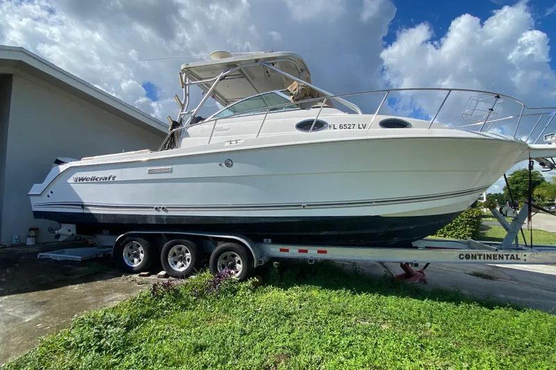 Slide: The Image of 2002 Wellcraft 290 Coastal boat on trailer, parked outdoors under a cloudy sky. - 11