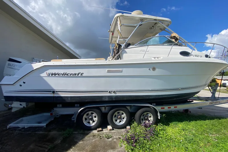 Slide: The Image of 2002 Wellcraft 290 Coastal boat on trailer, parked outdoors under a cloudy sky. - 15