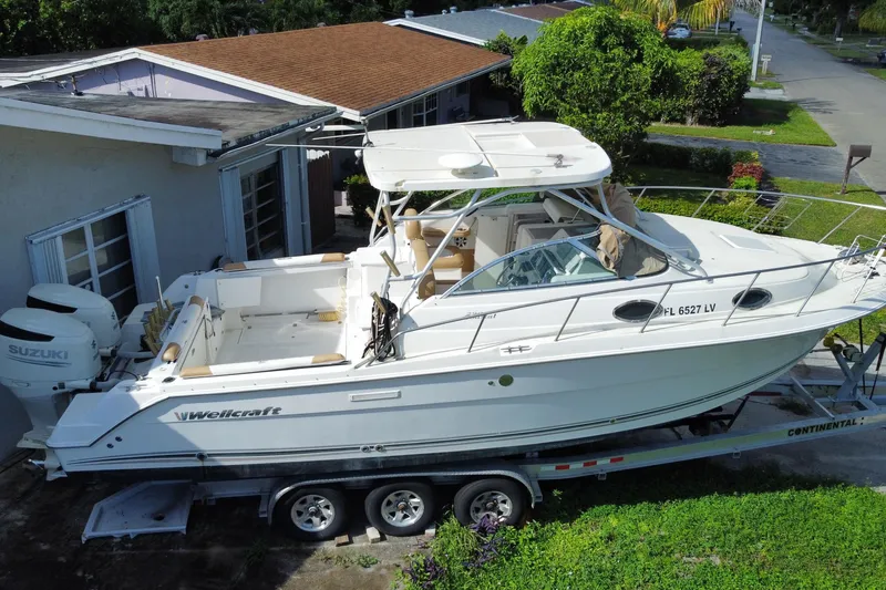 Slide: The Image of 2002 Wellcraft 290 Coastal boat on trailer, parked beside a house, featuring Suzuki outboard engines. - 3