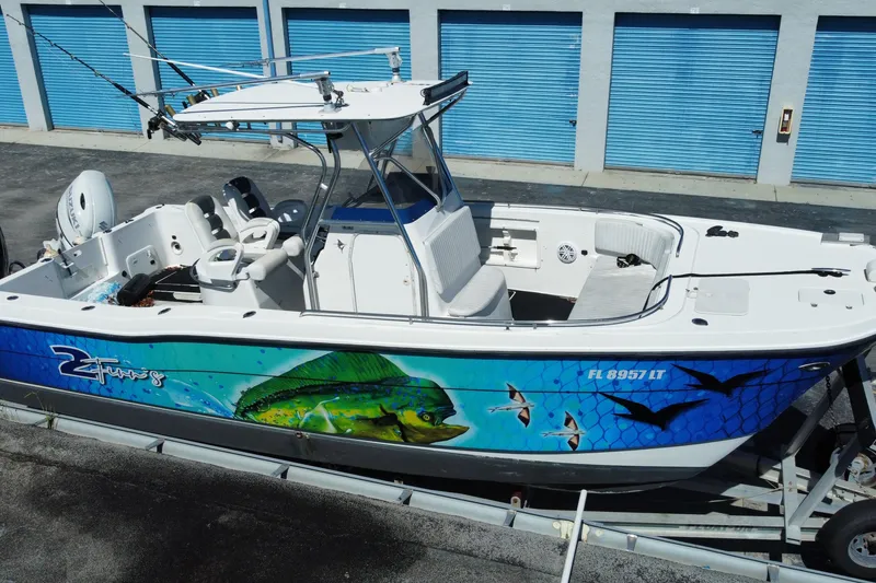 Slide: The Image of 2002 ProKat 2660 Center Console boat with vibrant marine graphics, parked near blue storage units. - 12